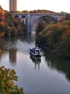 a boat traveling down a river next to a bridge in the middle of trees with fall foliage