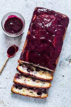 sliced loaf of bread with blueberry jam on top next to jar of jelly and spoon