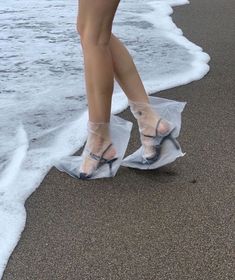 a woman's legs in clear plastic shoes on the beach