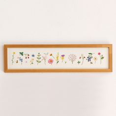 a wooden frame with flowers on it hanging from the wall next to a white wall