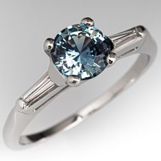 an engagement ring with a blue diamond and two baguets on the side, in white gold