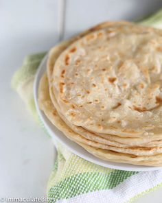 a stack of tortillas sitting on top of a white plate next to a green and white towel