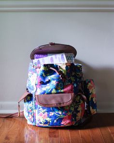 a floral backpack sitting on top of a hard wood floor next to a white wall