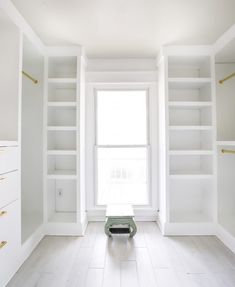 an empty room with white bookcases and a bench in the middle of it