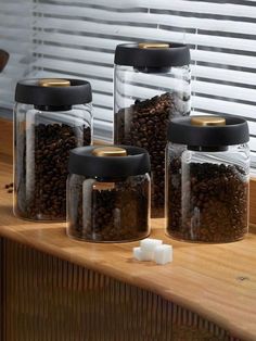 three glass jars filled with coffee beans and marshmallows on top of a wooden counter