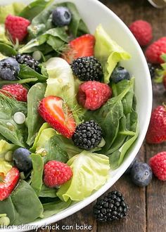 a salad with berries, lettuce and spinach in a white bowl on a wooden table