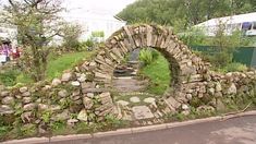 an old stone arch is in the middle of a road with people standing around it