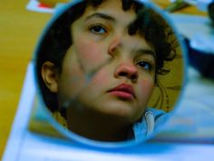 a young boy looking at his reflection in a mirror with blue eyes and curly hair