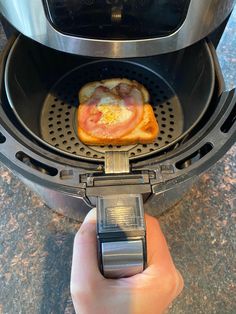 a toaster with an egg and ham in it being held by a person's hand