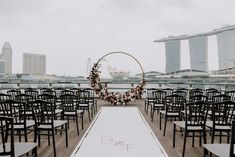 an outdoor ceremony setup with black chairs and floral arrangements on the aisle, in front of large cityscape