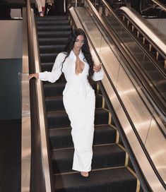 a woman is walking down an escalator in a white dress