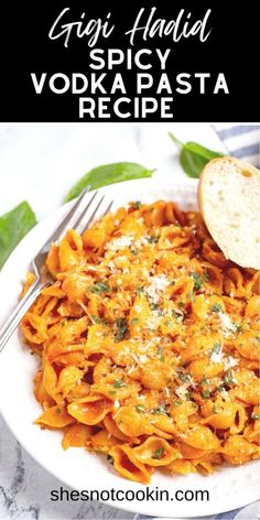 a white plate topped with pasta covered in sauce and parmesan cheese next to a slice of bread