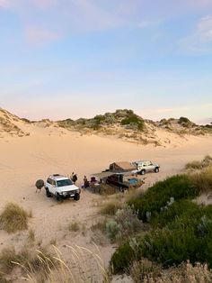 an suv is parked in the sand with other vehicles and people standing around it near some bushes