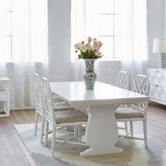 a white dining room table with chairs and a vase filled with flowers on top of it