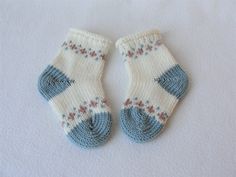 two knitted baby socks with blue and white designs on them sitting on a bed