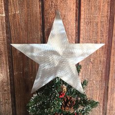 a white star hanging from the side of a wooden wall with pine cones and berries