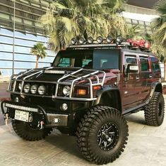 a red hummer truck parked in front of a building with palm trees on the side