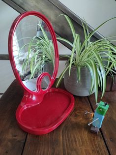 a red heart shaped mirror sitting on top of a wooden table next to a potted plant