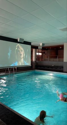 two people in a swimming pool watching a movie on the wall behind them is a projector screen