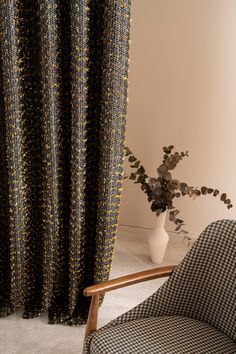 a black and yellow patterned curtain next to a chair with a vase on the floor