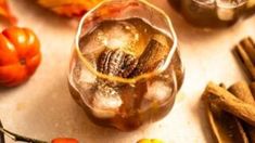 a glass filled with ice sitting on top of a table next to some pumpkins