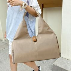 a woman carrying a large beige bag on her shoulder