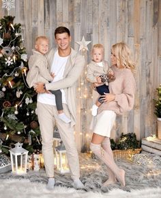 a man and woman holding two children in front of a christmas tree with lights on it