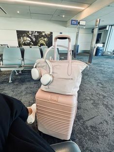 a woman is sitting in an airport with her suitcase and headphones attached to it