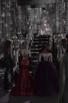 three women in evening gowns are walking up the stairs to an elaborate staircase area