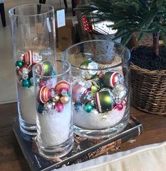 three glass vases filled with ornaments on top of a wooden table next to a christmas tree