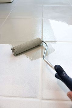 a person using a roller to paint a tile floor with white grouting on it