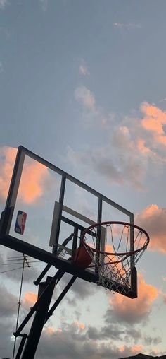 a basketball hoop with the sun setting in the background and clouds above it, as seen from below