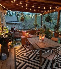 an outdoor dining area with lights strung from the ceiling and potted plants on the table