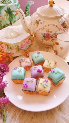 some cupcakes are sitting on a plate next to a teapot and flowers