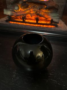 a black vase sitting on top of a table next to a fire in a fireplace