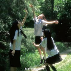 four girls in school uniforms are playing with a frisbee on a path through the woods