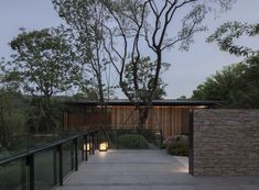 an outdoor walkway leading to a house with trees in the back ground and lights on