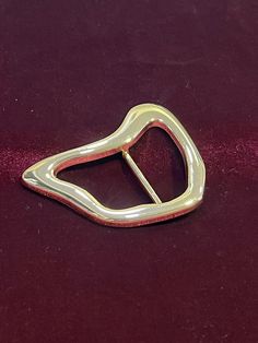 a gold colored metal buckle on a red velvet surface with the clasp partially closed to reveal a square shape