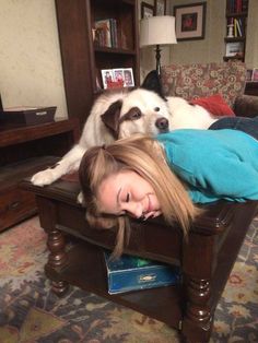 a woman laying on top of a wooden bed next to a white dog in a living room