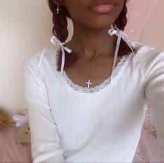 a woman in white shirt sitting on bed with teddy bear and pink wall behind her