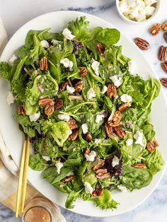 a white plate topped with lettuce salad next to a bowl of nuts and dressing