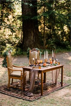 a table set up with candles and other items for an outdoor dinner party in the woods