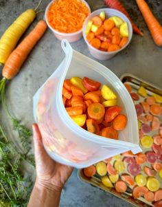 a person holding up a plastic container filled with carrots and other vegetables next to some food