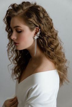 a woman with long hair wearing earrings and a white dress is looking down at her left shoulder