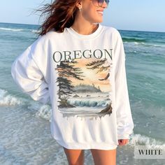 Our Oregon Pacific Northwest Sweatshirt--a cozy homage to the rugged charm of the Pacific Northwest! Crafted for comfort and warmth, this sweatshirt features a captivating watercolor scene of an Oregon sunset beachscape, complete with crashing waves, lush trees, and a soaring bald eagle.  Whether you're hiking, camping, or simply seeking a reminder of Oregon's wild beauty, this sweatshirt is the perfect companion. Embrace the spirit of the Pacific Northwest and carry a piece of its untamed allure with you wherever you go! .: Fabric blends: Heather Sport colors - 60% polyester, 40% cotton .: All others 50% cotton, 50% polyester .: Medium-heavy fabric (warm and cozy) .: Unisex loose fit - Please reference the size chart in the photos or feel free to reach out to me with any sizing questions! White Cotton Sweater For Outdoor, White Casual Sweater For Outdoor, White Relaxed Fit Sweatshirt For Outdoor Activities, Oregon Sunset, Pacific Northwest Style, Beach Pullover, Wardrobe Makeover, Wild Beauty, Crashing Waves