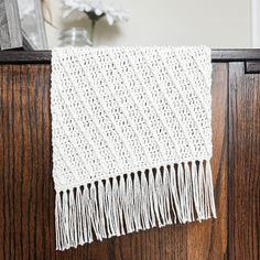 a white crocheted blanket hanging on a wooden dresser next to a vase with flowers