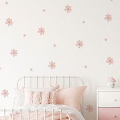 a white bed sitting next to a pink dresser under a wall with flowers on it