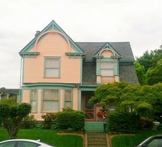 two cars are parked in front of a pink house with green trees and bushes on both sides