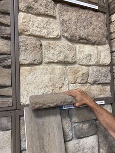 a man is holding up a stone block to the side of a brick wall with signs on it