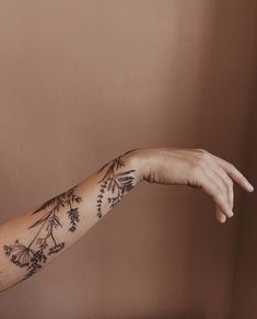 a woman's arm with flowers and leaves on it, in front of a brown wall